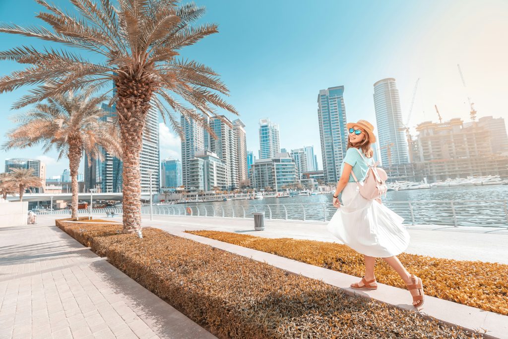 Female traveller walks beside the water in the UAE with tall buildings in the background