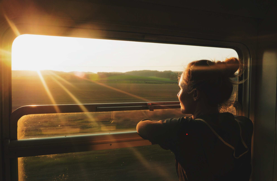 Woman gazes out of train window at sunset over a landscape in Algeria