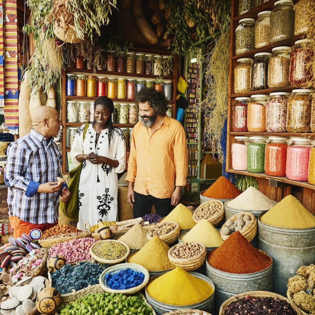 Wide shot of couple talking to shop owner while shopping in spice shop in the souks of Marrakech during vacation