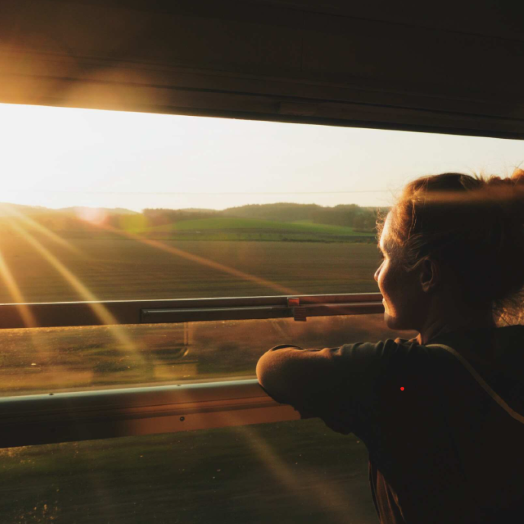Woman gazes out of train window at sunset over a landscape in Algeria