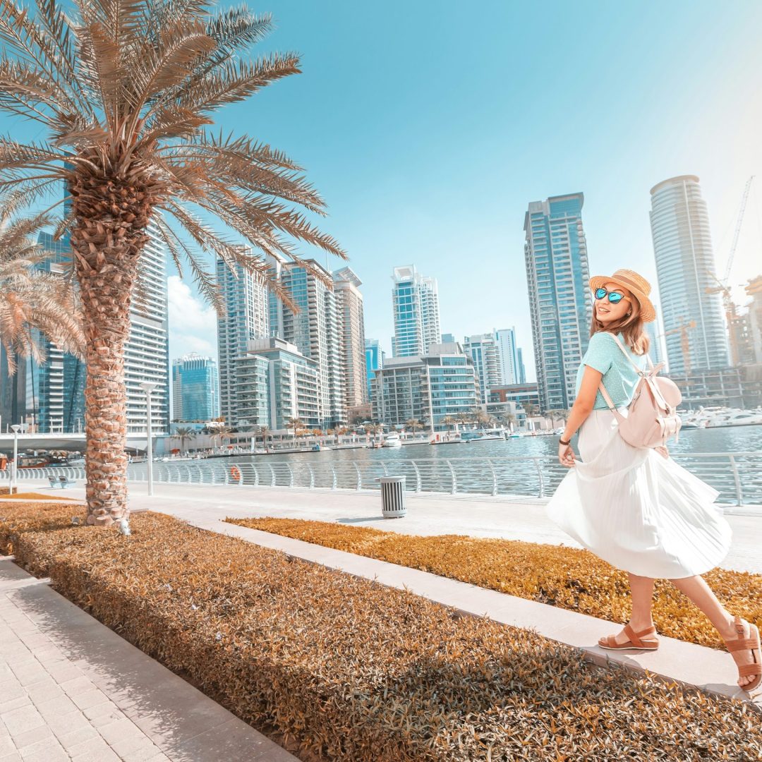 Female traveller walks beside the water in the UAE with tall buildings in the background